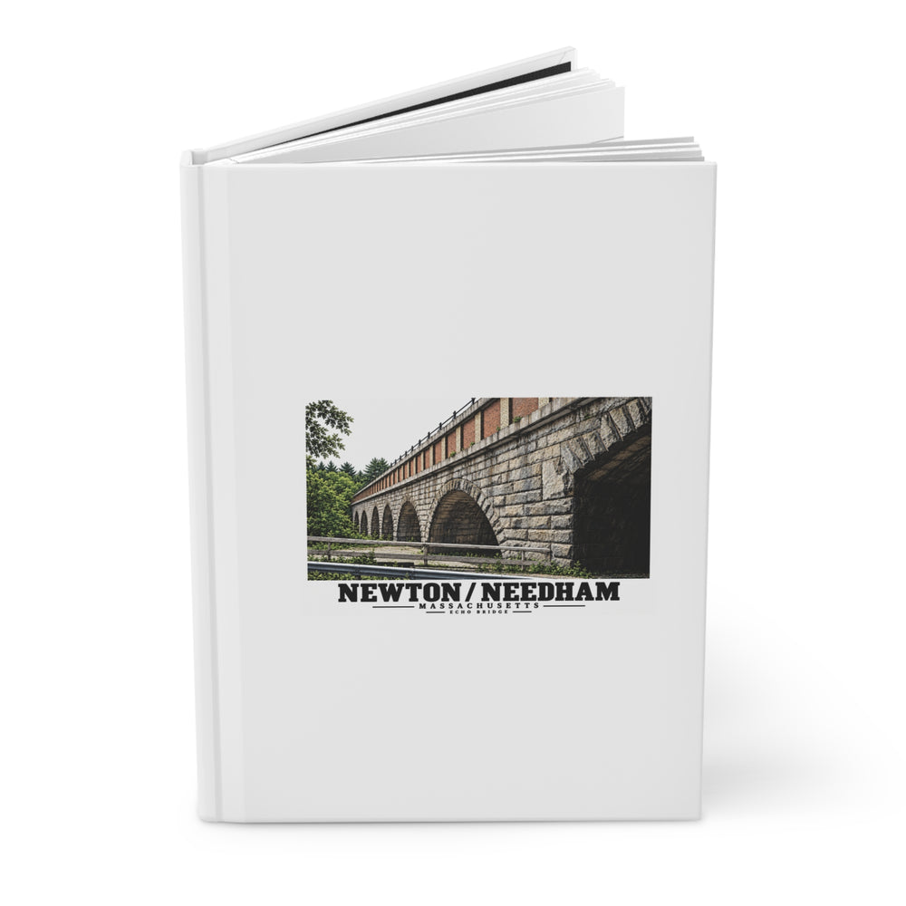 Partly opened white hardcover journal with Echo Bridge artwork showing a row of stone arches and a brick upper band, with Newton/Needham lettering on its front cover.
