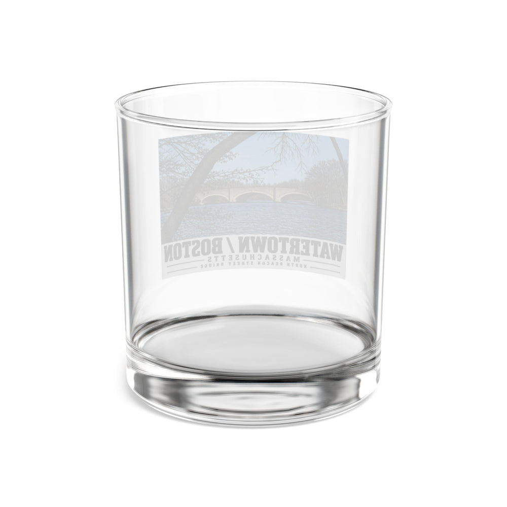 Rear view of clear rocks glass with North Beacon Street Bridge stone arches framed by a bare tree print and reversed lettering visible through the glass