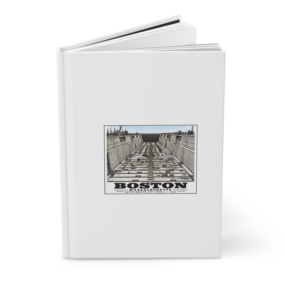 Partly opened white hardcover journal showing naval dry dock with concrete walls and rows of floor blocks artwork on the front