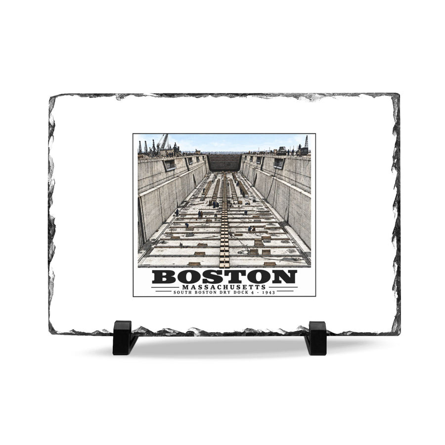 Rough-edged slate display on two black stands with naval dry dock with concrete walls and rows of floor blocks artwork and Boston lettering
