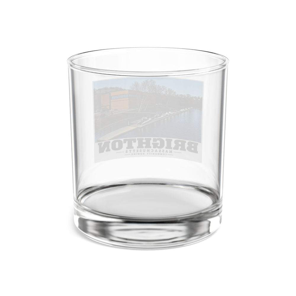 Rear view of clear rocks glass with Community Rowing building, dock and boats print and reversed lettering visible through the glass
