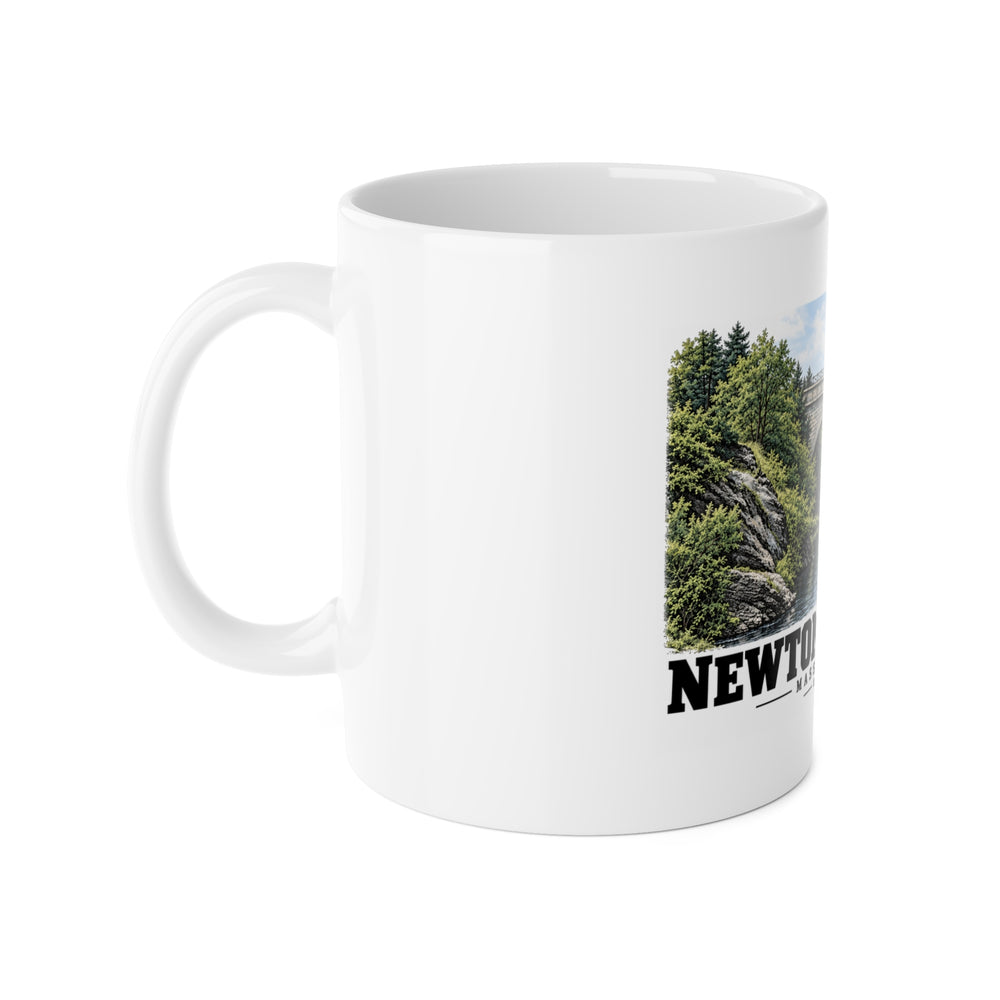 White ceramic mug with its handle on the left and part of the Echo Bridge artwork showing a stone arch over a river and trees, with Newton/Needham lettering visible on the right.