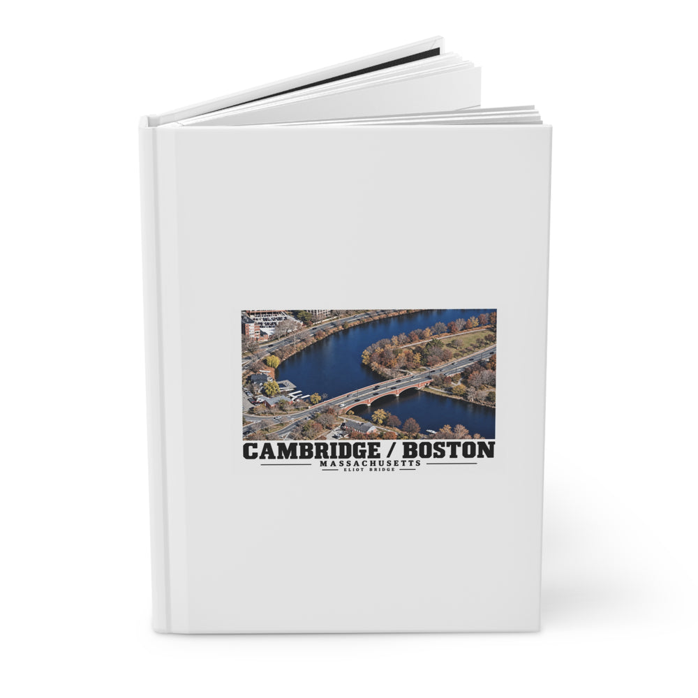 Partly opened white hardcover journal showing Eliot Bridge aerial river view artwork on the front