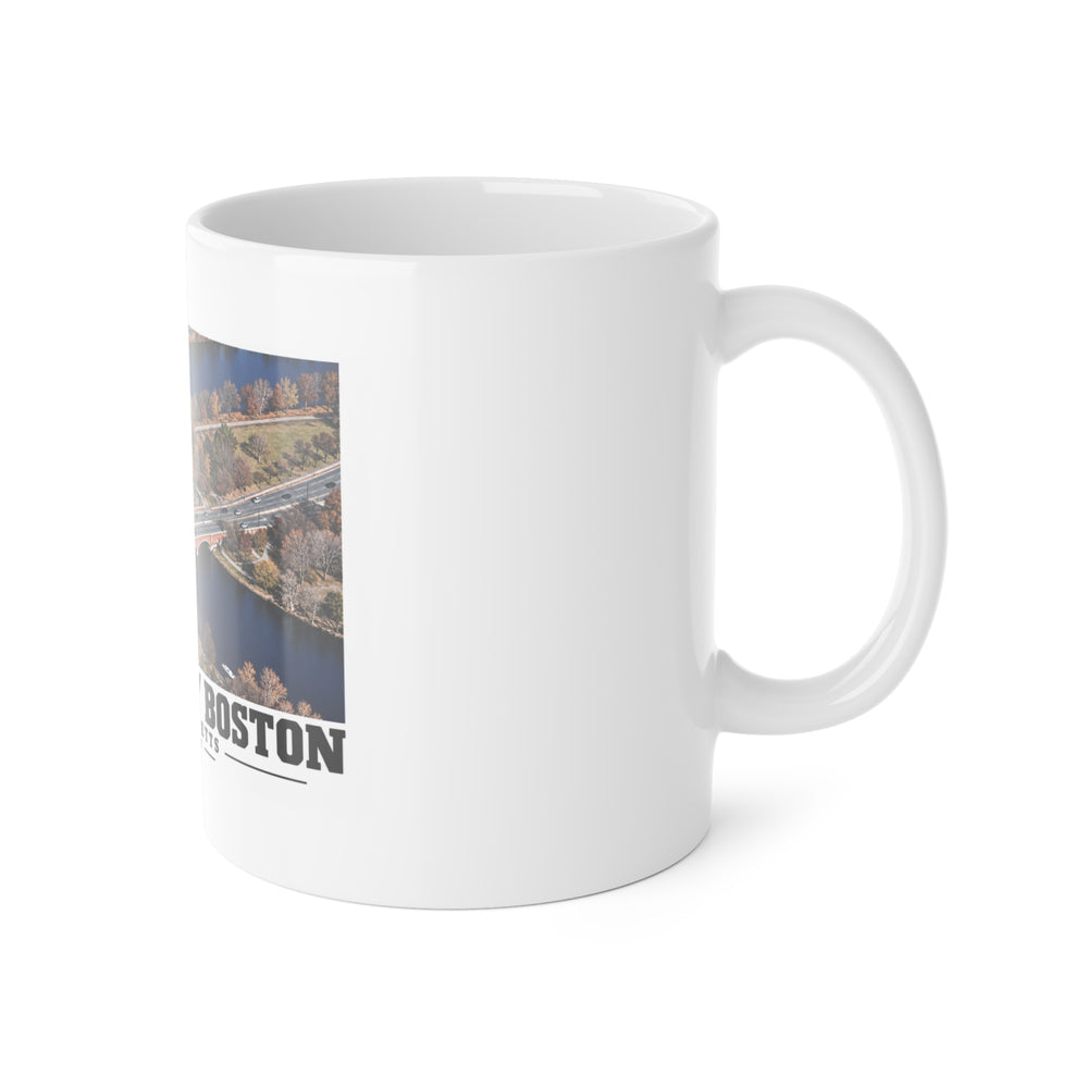 White mug with handle at right and part of the Eliot Bridge aerial river view print at left