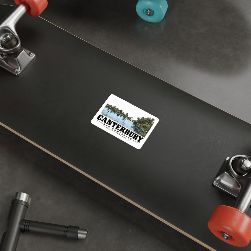 Skateboard display of Shaker turning mill and pond white die-cut sticker, with Canterbury, New Hampshire artwork and lettering.