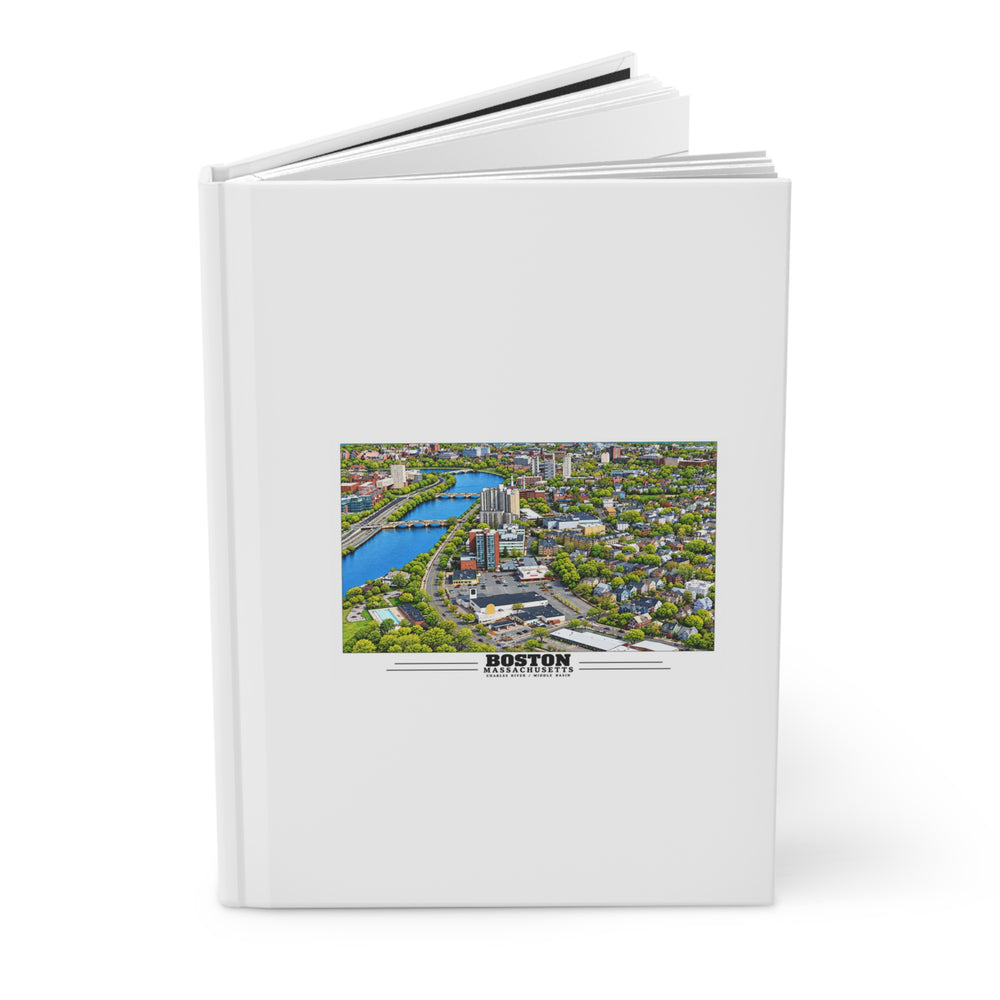 Partly opened white hardcover journal showing Charles River aerial city view with bridges, buildings and green trees artwork on the front