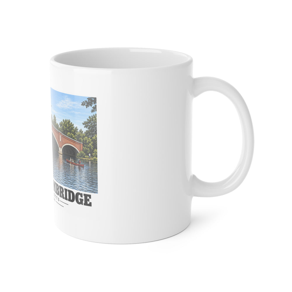 White mug with handle at right and part of the Eliot Bridge red brick arches and boats print at left