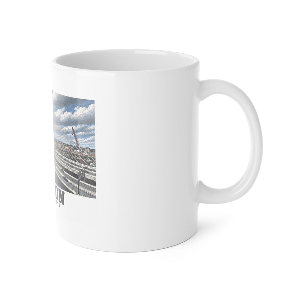 White mug with handle at right and part of the Zakim Bunker Hill Bridge cable-stayed towers and Charles River print at left