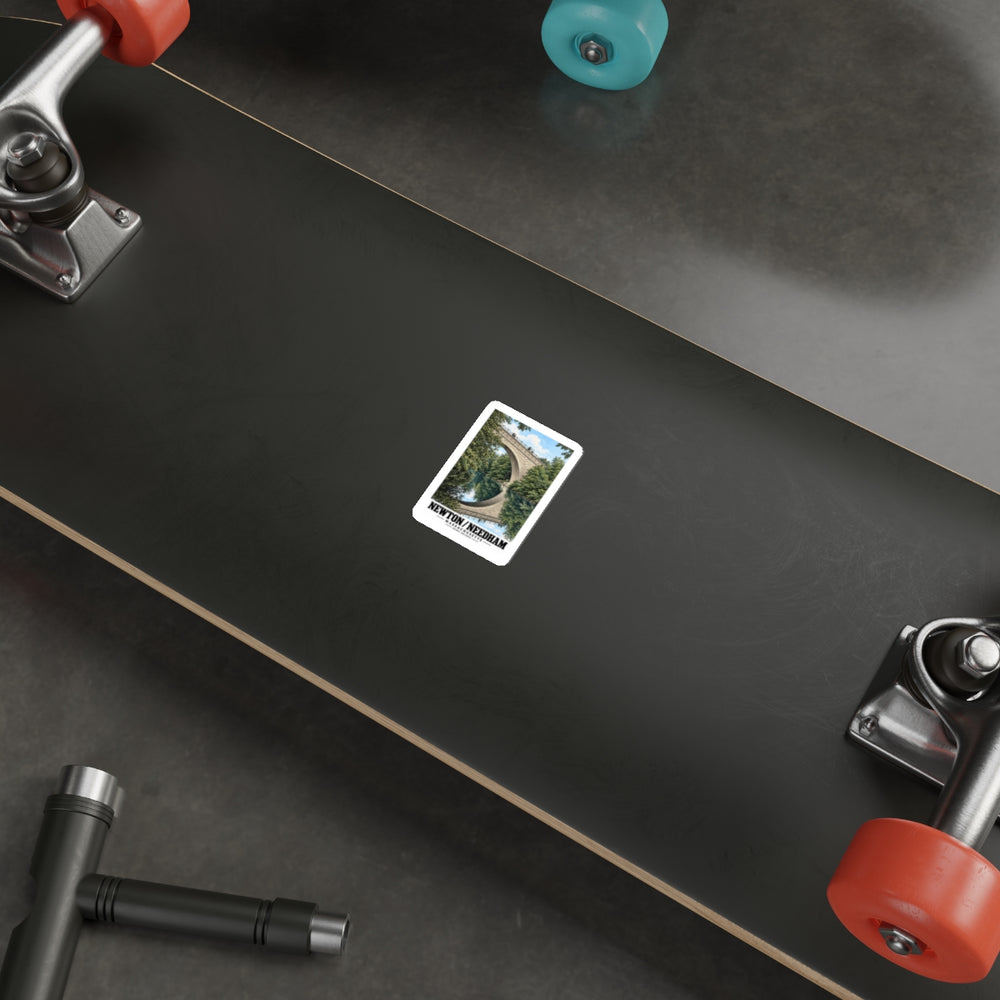 Sticker showing Echo Bridge portrait view of the stone arch and its reflection with Newton/Needham lettering on the underside of a black skateboard with metal trucks and colored wheels