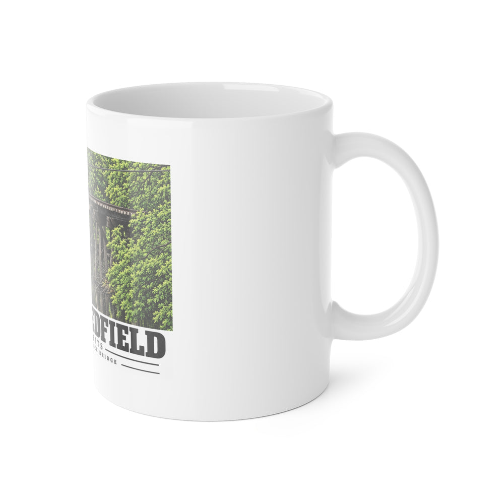 White mug with handle at right and part of the Millis Industrial Track wooden railway trestle and green foliage print at left