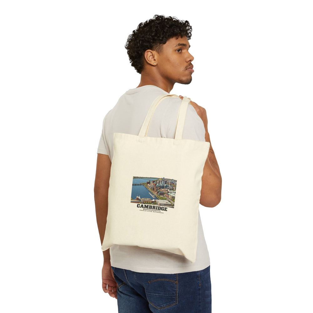 Person carrying a natural tote over one shoulder with Cambridge Charles River waterfront aerial city view print visible