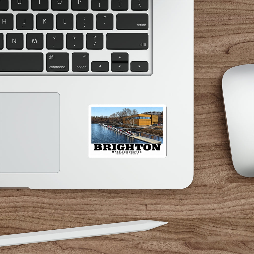 Sticker showing Community Rowing building, dock and boats artwork on a laptop beside its keyboard