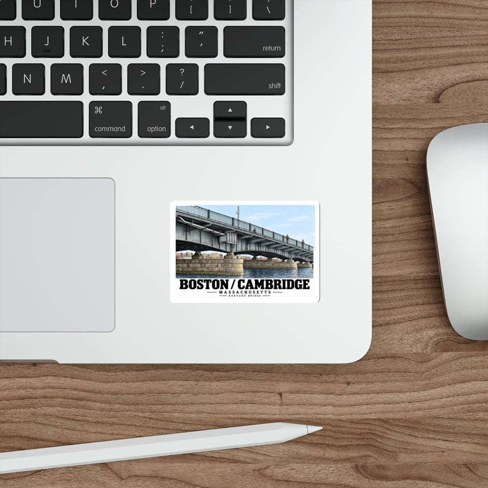 Sticker showing Harvard Bridge close girder view with Boston/Cambridge lettering on a laptop palm rest beside the trackpad on a wood desk