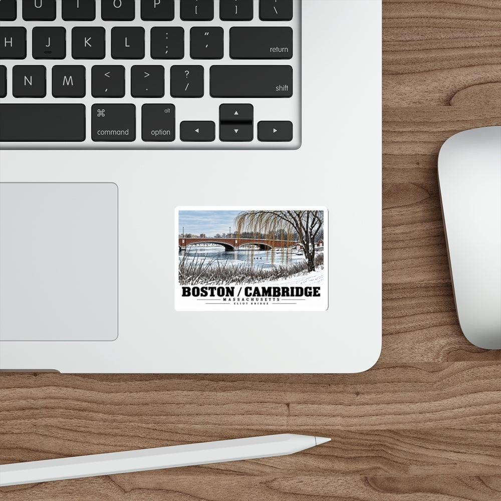 Sticker showing Eliot Bridge winter river view with snow and bare trees artwork on a laptop beside its keyboard