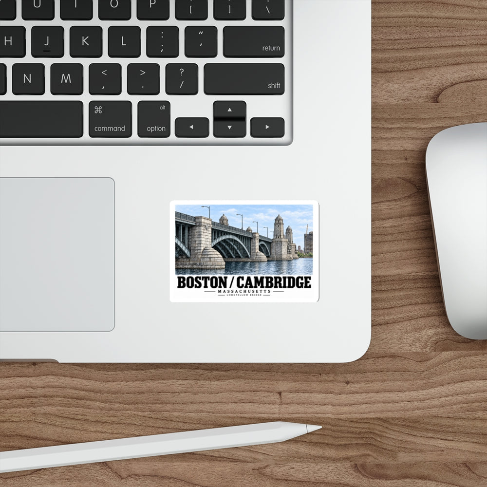 Sticker showing Longfellow Bridge piers and towers with Boston/Cambridge lettering on a laptop palm rest beside the trackpad on a wood desk