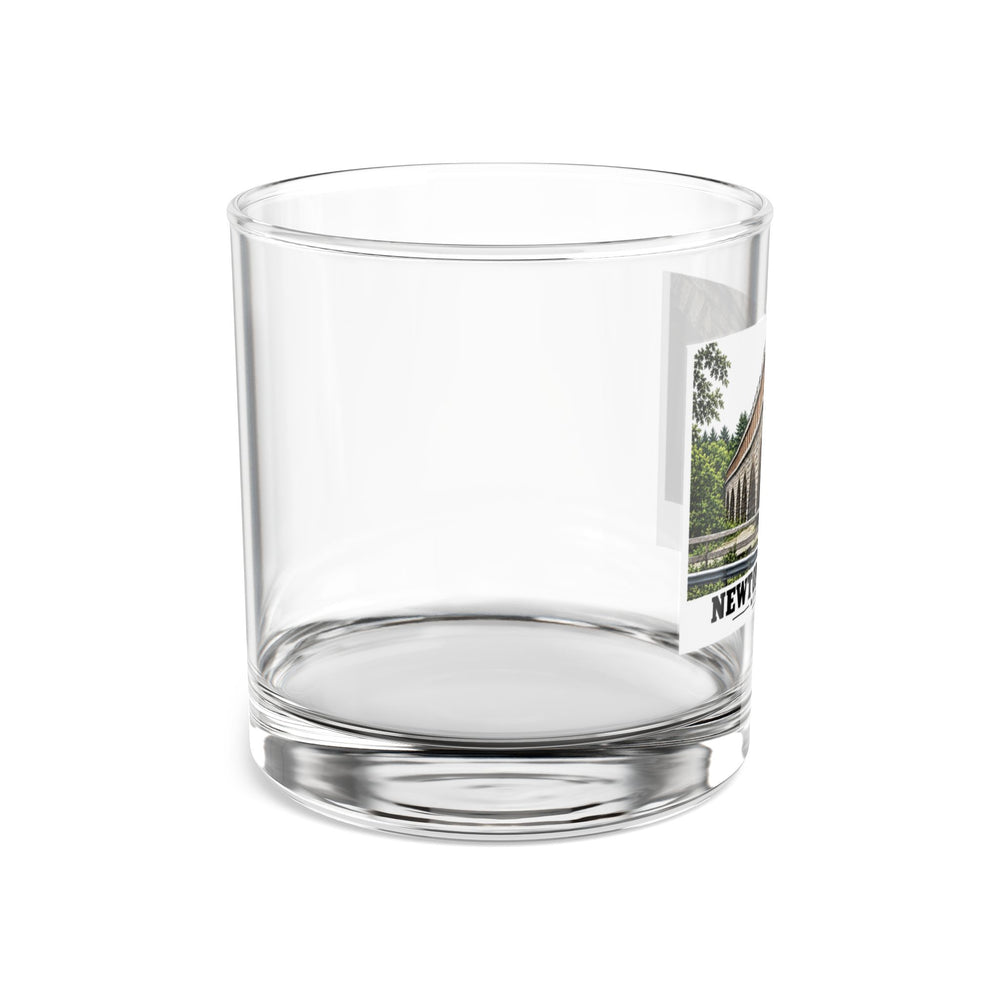 Side view of a clear rocks glass with part of the Echo Bridge artwork showing a row of stone arches and a brick upper band, with Newton/Needham lettering visible on the right.