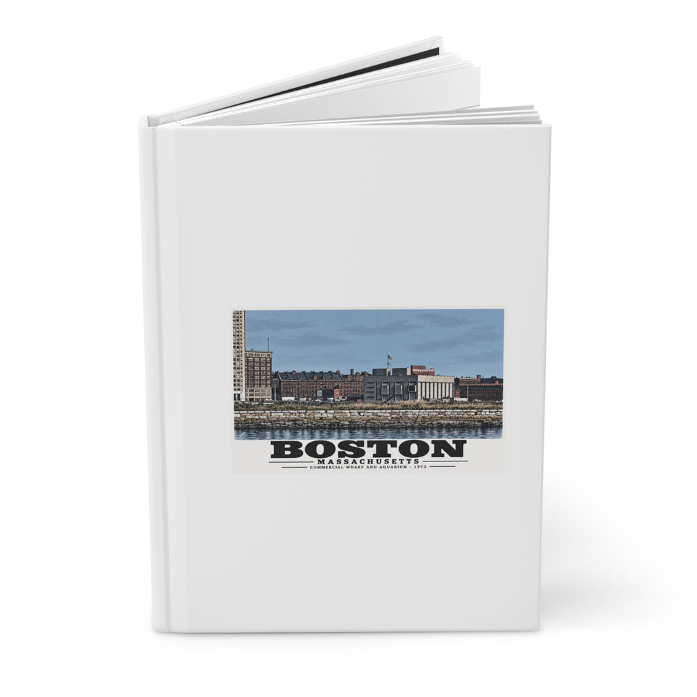 Partly opened white hardcover journal showing Commercial Wharf and Aquarium waterfront buildings, stone seawall and harbor water artwork on the front
