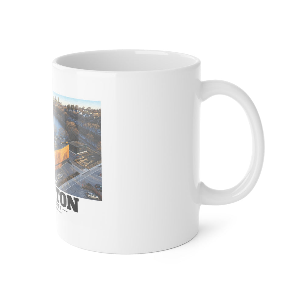 White mug with handle at right and part of the Community Rowing aerial building and river print at left