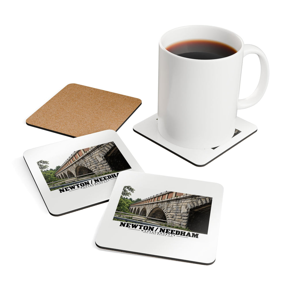 Square coasters showing printed fronts with Echo Bridge artwork showing a row of stone arches and a brick upper band, with Newton/Needham lettering and a plain cork reverse, with a white mug resting on one coaster.