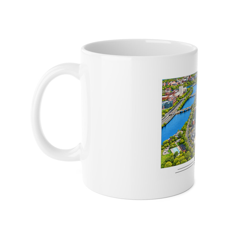 White mug with handle at left and part of the Charles River aerial city view with bridges, buildings and green trees print at right