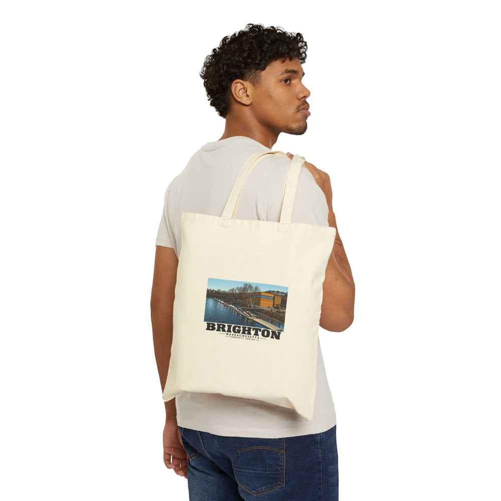 Person carrying a natural tote over one shoulder with Community Rowing building, dock and boats print visible