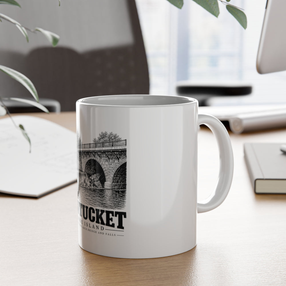 Pawtucket Main Street Stone-Arch Bridge and Falls — White 11-ounce ceramic mug, on desk with handle visible.